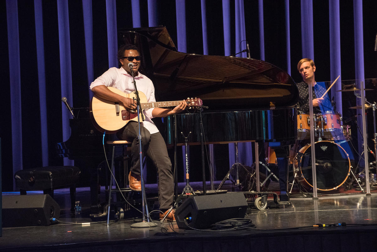 Blessing Offor sits on a stool playing a guitar on the Kennedy Center's Millennium Stage