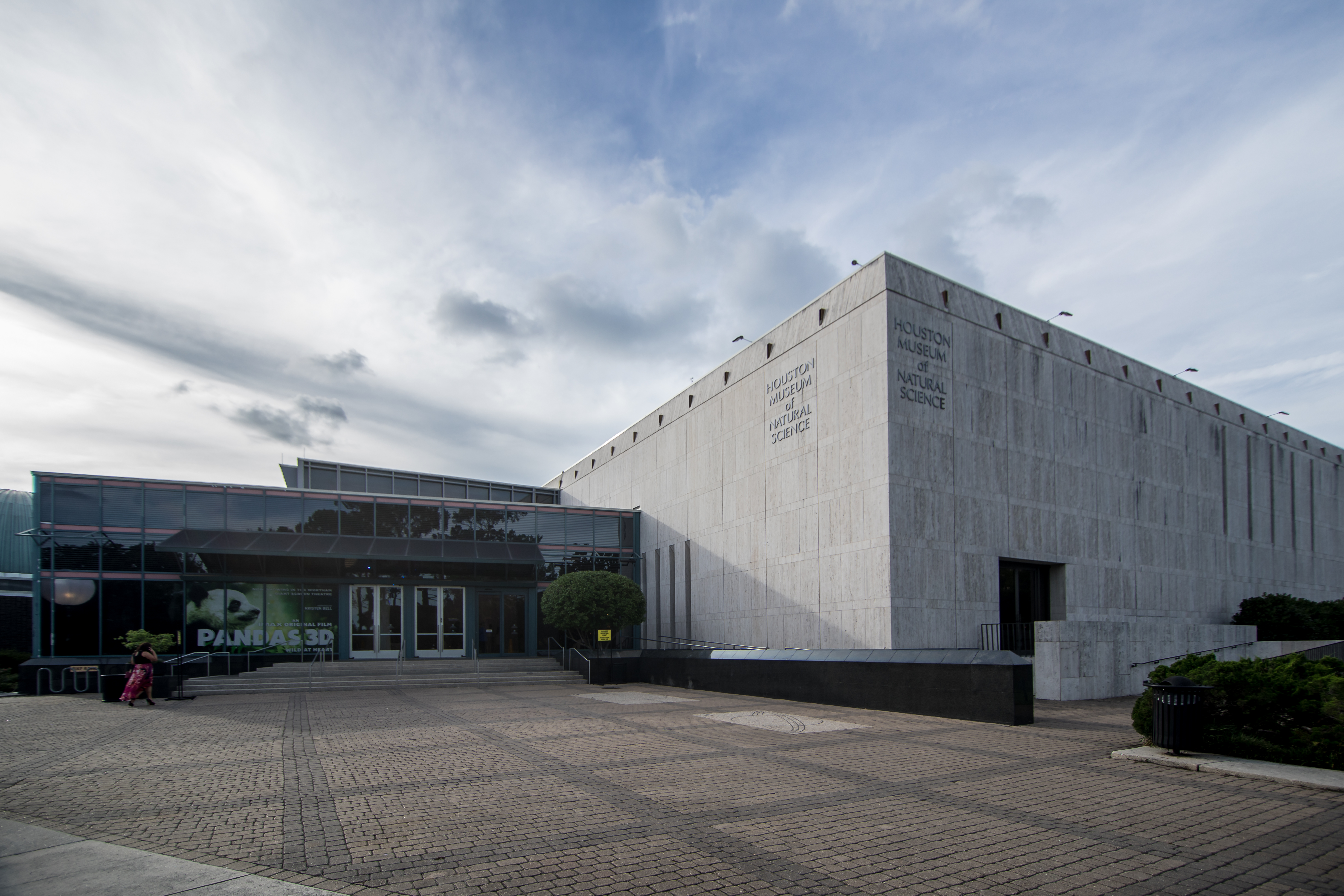 A concrete building in front of a partially cloudy sky. Letters on the building read 