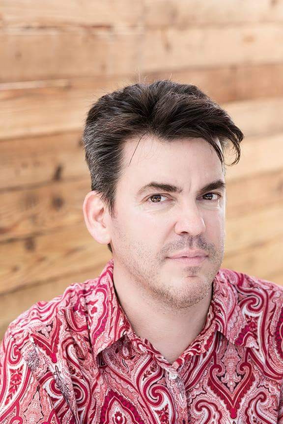 A picture of Greg Walloch, a white man with shirt, brown hair, wearing a red and white patterned collared shirt