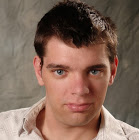 [Image Description:  A photo of a man with short brown hair and blue eyes.  He is wearing a white button up shirt and the background is grey.]