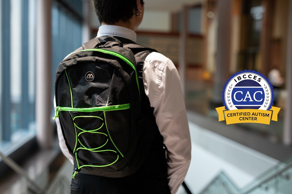 The back of a person standing with a black backpack with green zippers. A graphic of a badge to the right of the person reads 