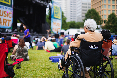 Woman in a wheelchair sitting on a lawn watching a music performance at a festival