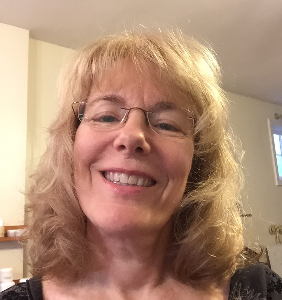 Photo of Deborah Nelson, a smiling woman with a fair complexion and shoulder-length blond hair. She wears rimless eyeglasses and a dark shirt